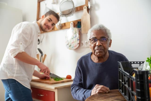 Young man assisting elderly man in wheelchair in kitchen
